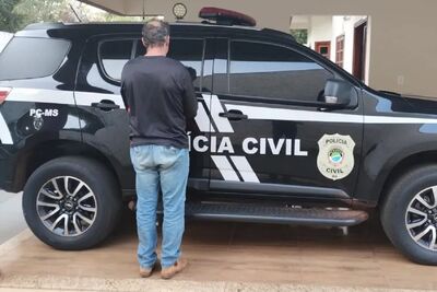 Suspeito do crime diante de viatura da Polícia Civil.