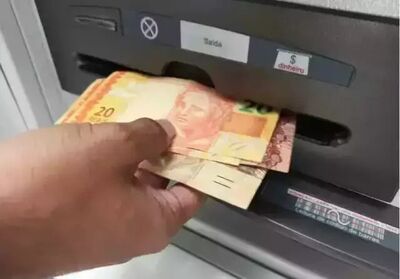 Pessoa saca cédulas de dinheiro em caixa eletrônico.