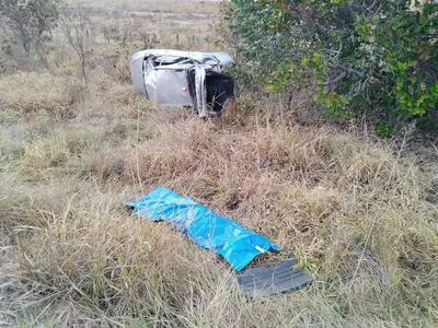 Carro destruído em vegetação e corpo da vítima coberto. 