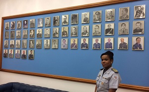 Helena Reis posa ao lado do quadro dos demais secretários da Casa Militar, em seu gabinete no Palácio dos Bandeirantes