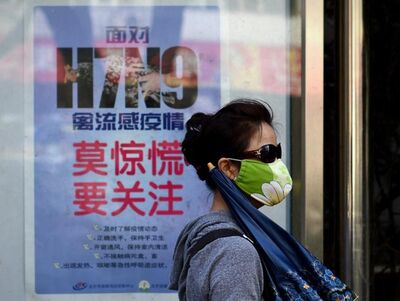 Usando máscara, mulher passa por cartaz com orientações contra a transmissão do vírus H7N9, em